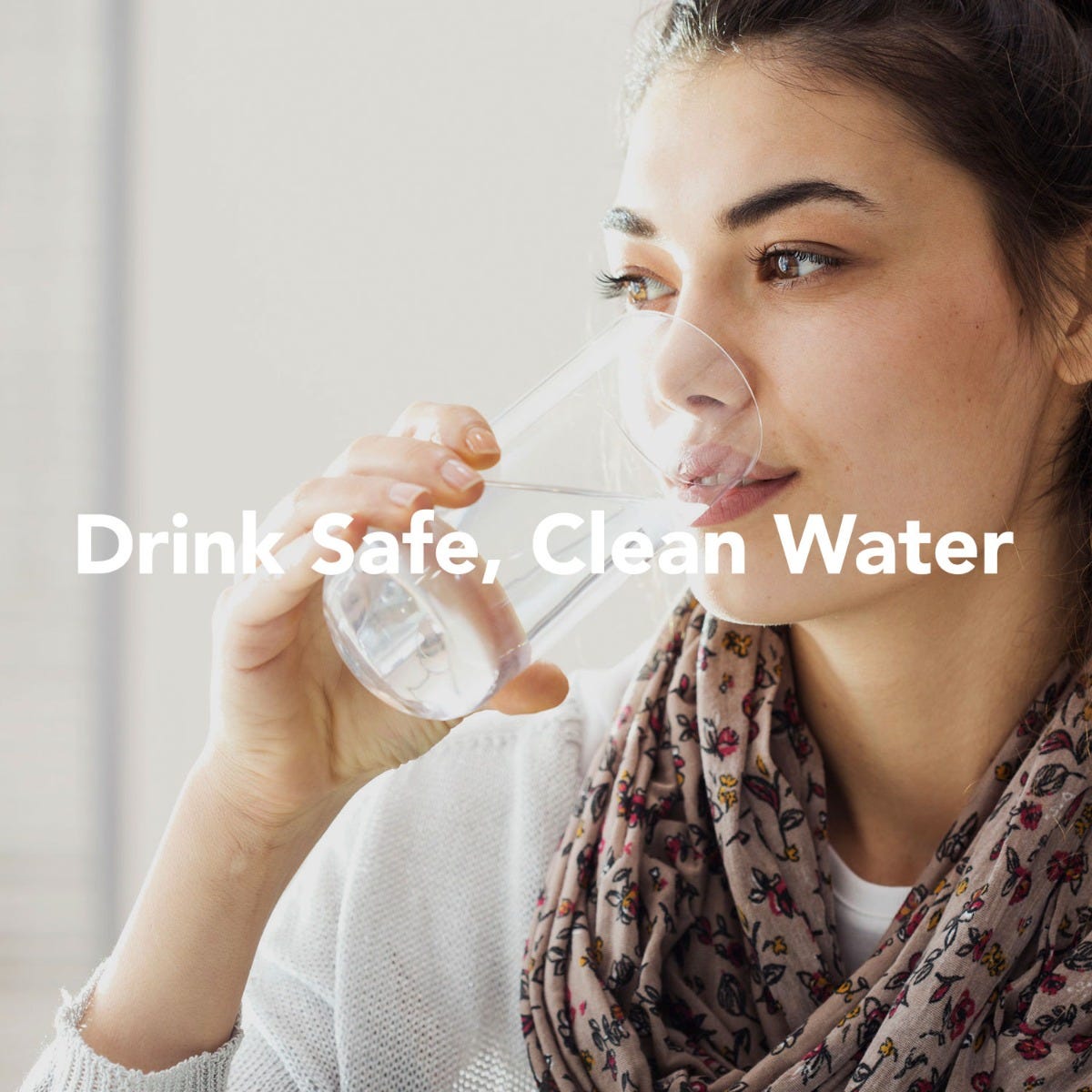 A person with long hair drinks water from a glass, wearing a scarf and light top. The text overlay states, Drink Safe, Clean Water. This image embodies the essence of quality offered by US Water Systems Incs American-Made 5 Stage Reverse Osmosis System. The background is softly blurred.