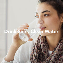 A person with long hair drinks water from a glass, wearing a scarf and light top. The text overlay states, Drink Safe, Clean Water. This image embodies the essence of quality offered by US Water Systems Incs American-Made 5 Stage Reverse Osmosis System. The background is softly blurred.